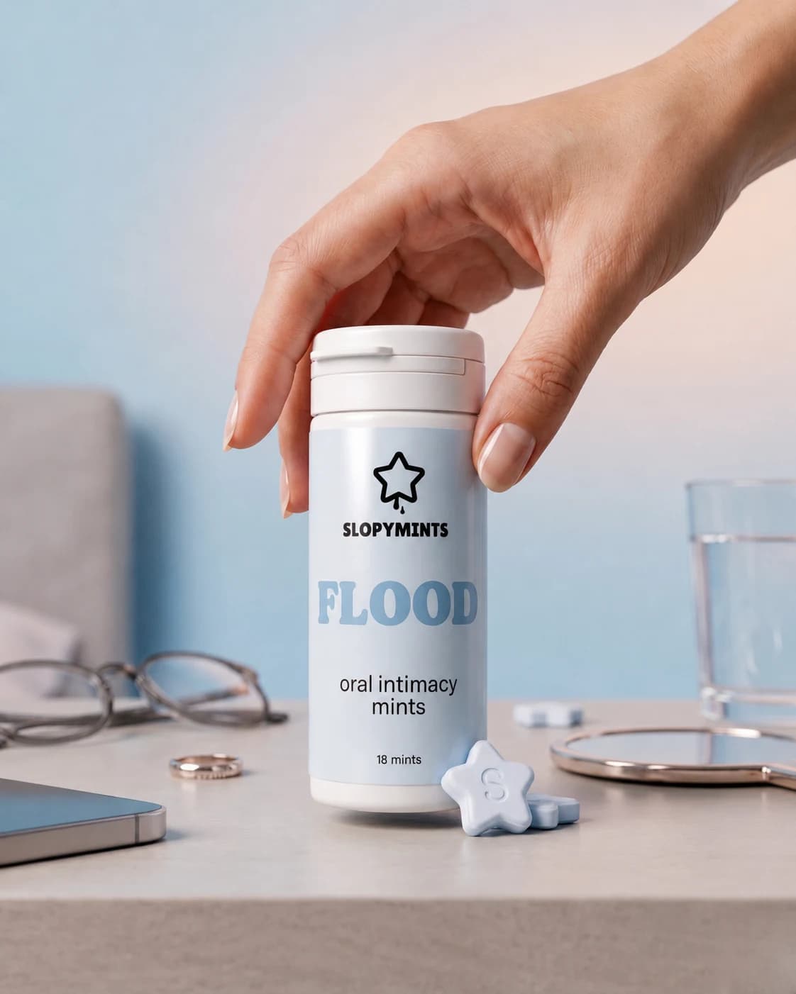 Hand picking up a tube of SlopyMints FLOOD on a bedside table